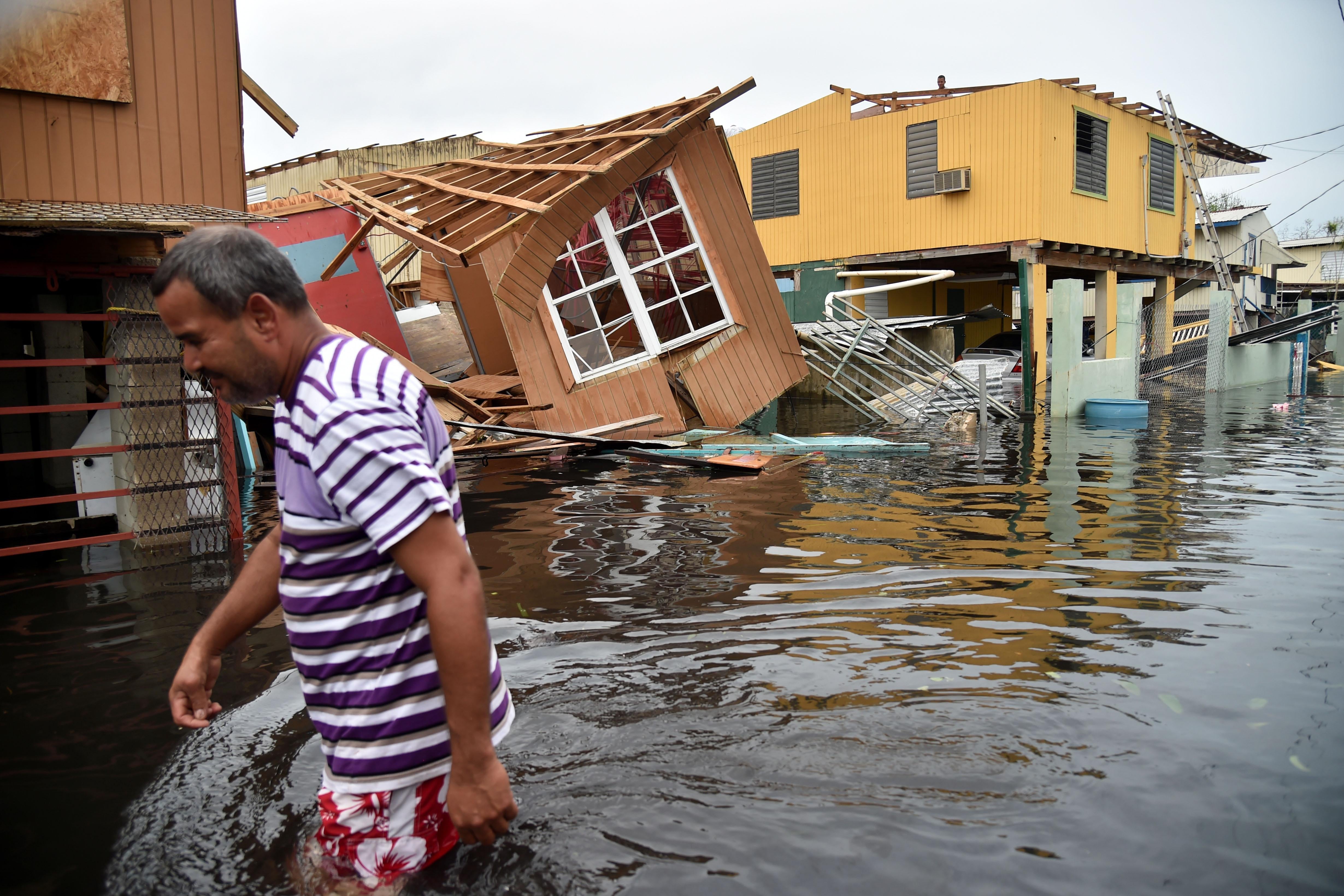 A man walks past a house laying in flood water 