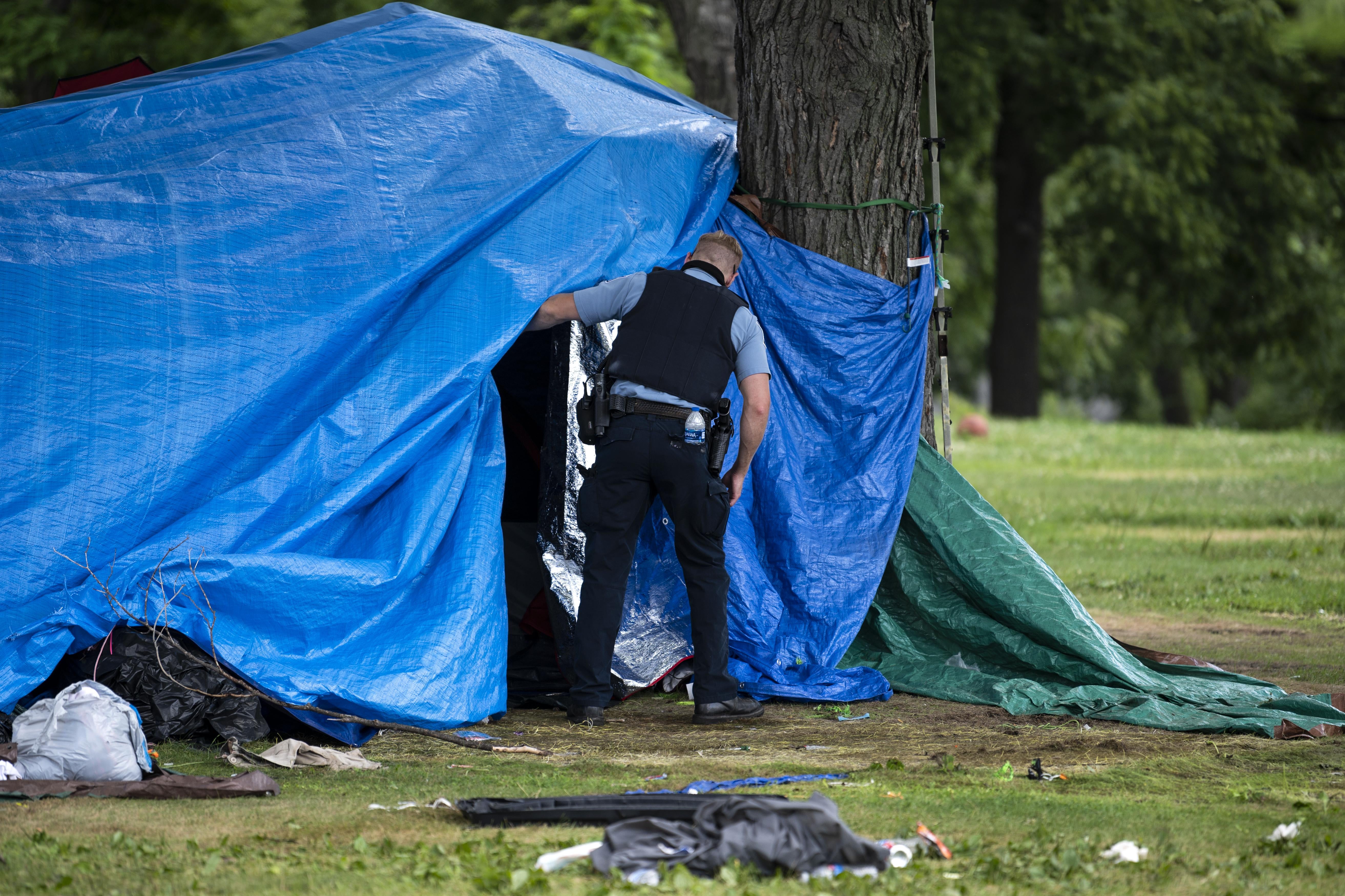 A man in a police uniform peers behind a tarp over a tent.