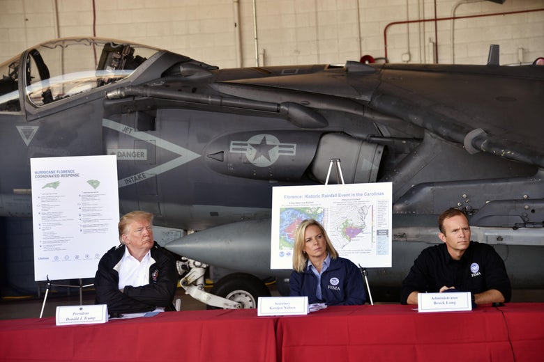 Donald Trump, Kristjen Nielsen, and Brock Long at a table in front of a military jet