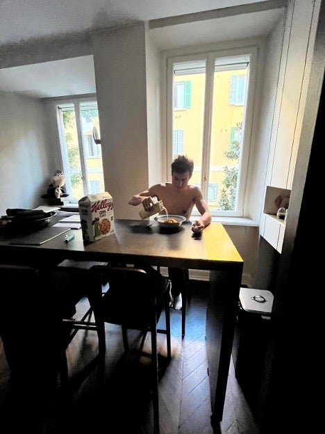 A man pours himself a bowl of corn flakes at a kitchen table.