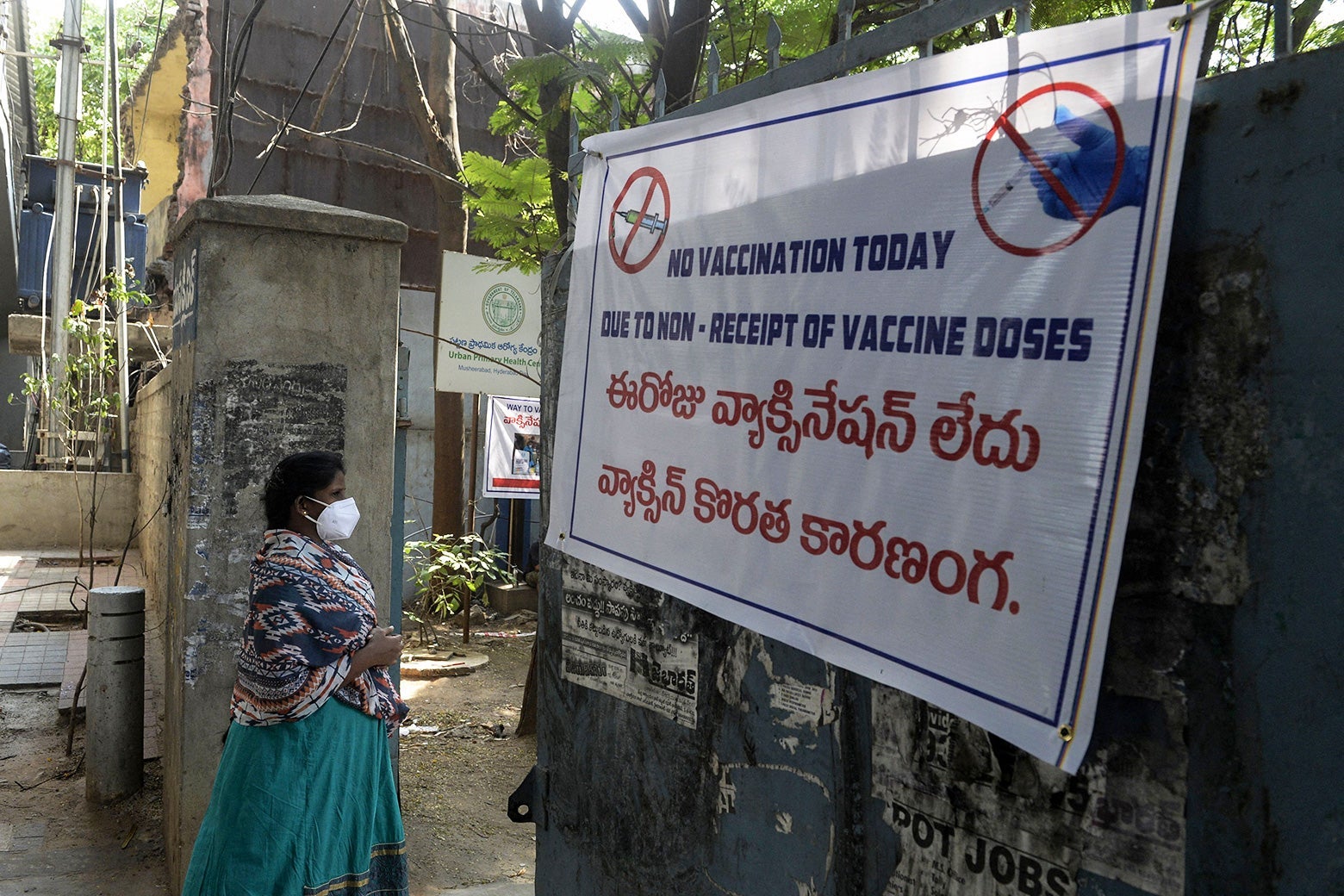 A woman walks past a sign reading "No vaccination today due to non-receipt of vaccine dose."