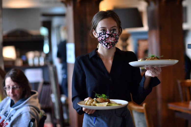 A woman carrying two plates and wearing a face mask