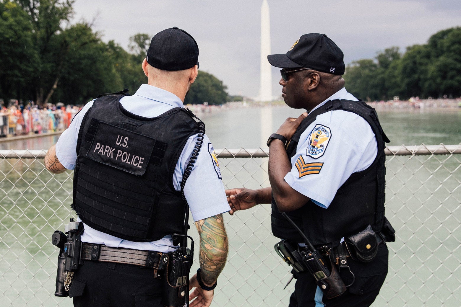 Two police officers chat in front of a chain-link fence with the reflecting pool and Washington Monument behind them.