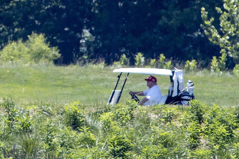 Trump in a golf cart with a MAGA hat on.