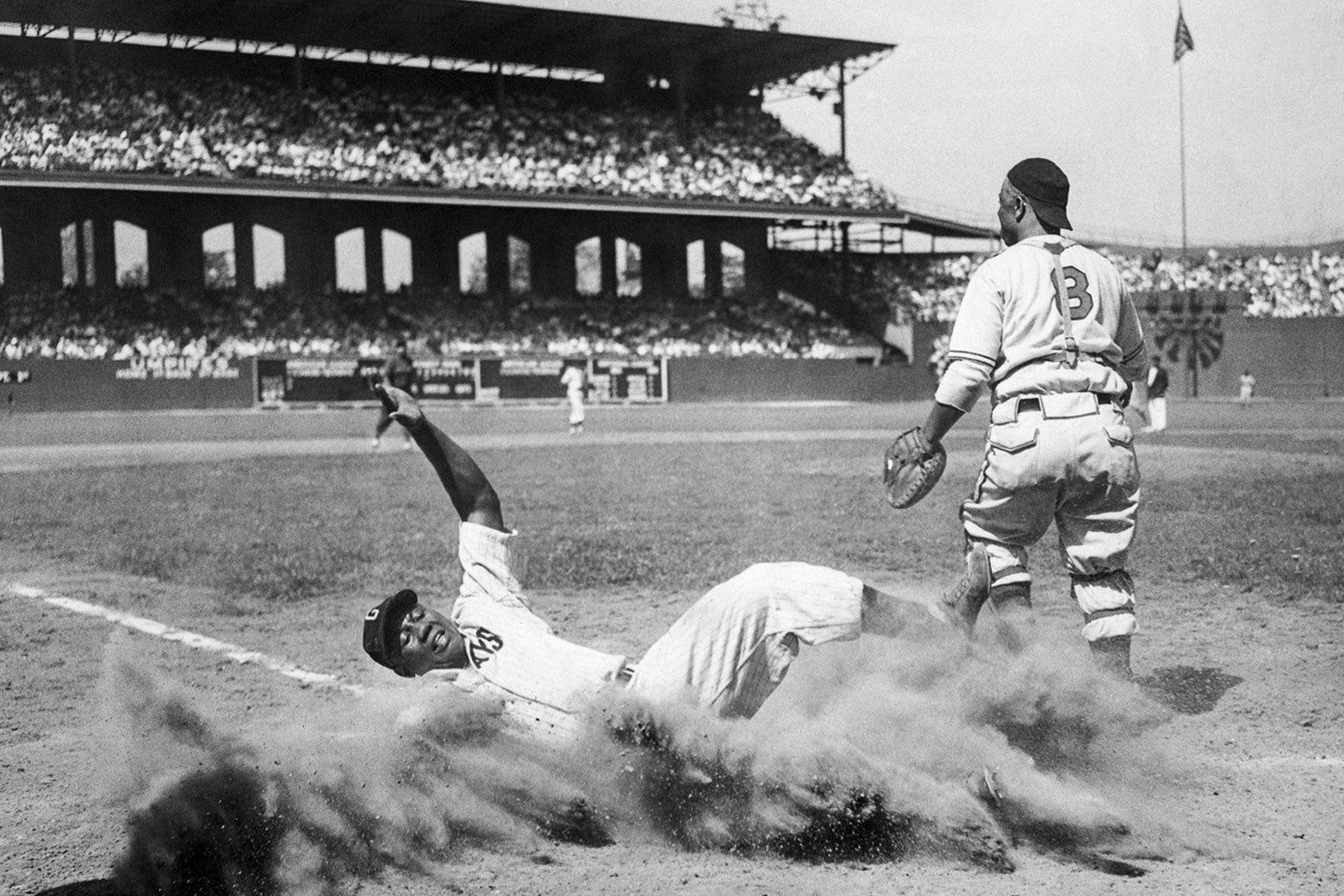 Josh Gibson slides into home, kicking up a cloud of dust at home plate, wincing