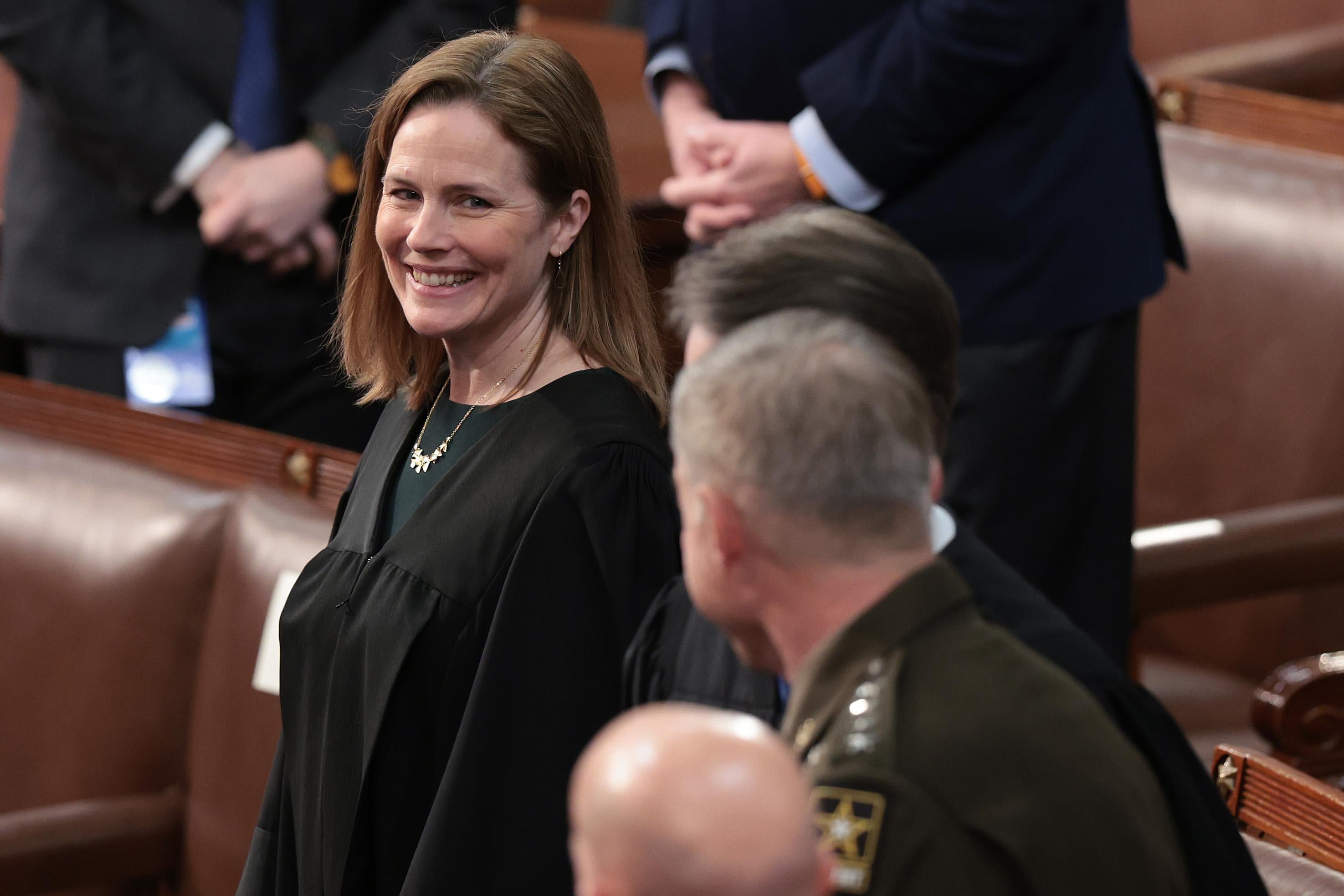 Barrett in her robes grinning as she stands in the House chamber