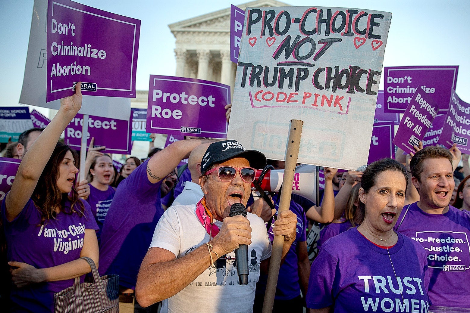 A crowd of protesters holding signs and wearing shirts with slogans such as "Trust Women," "Don't Criminalize Abortion," and "Protect Roe," with the Supreme Court in the background.