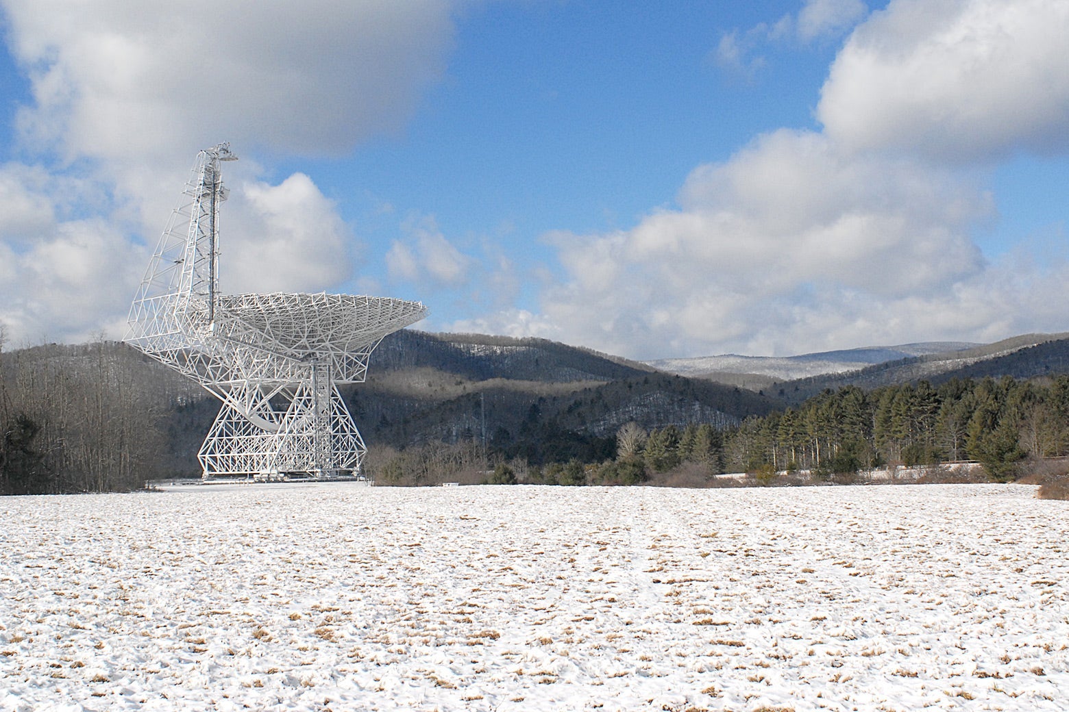 A large telescope in the middle of a field covered in light snow.