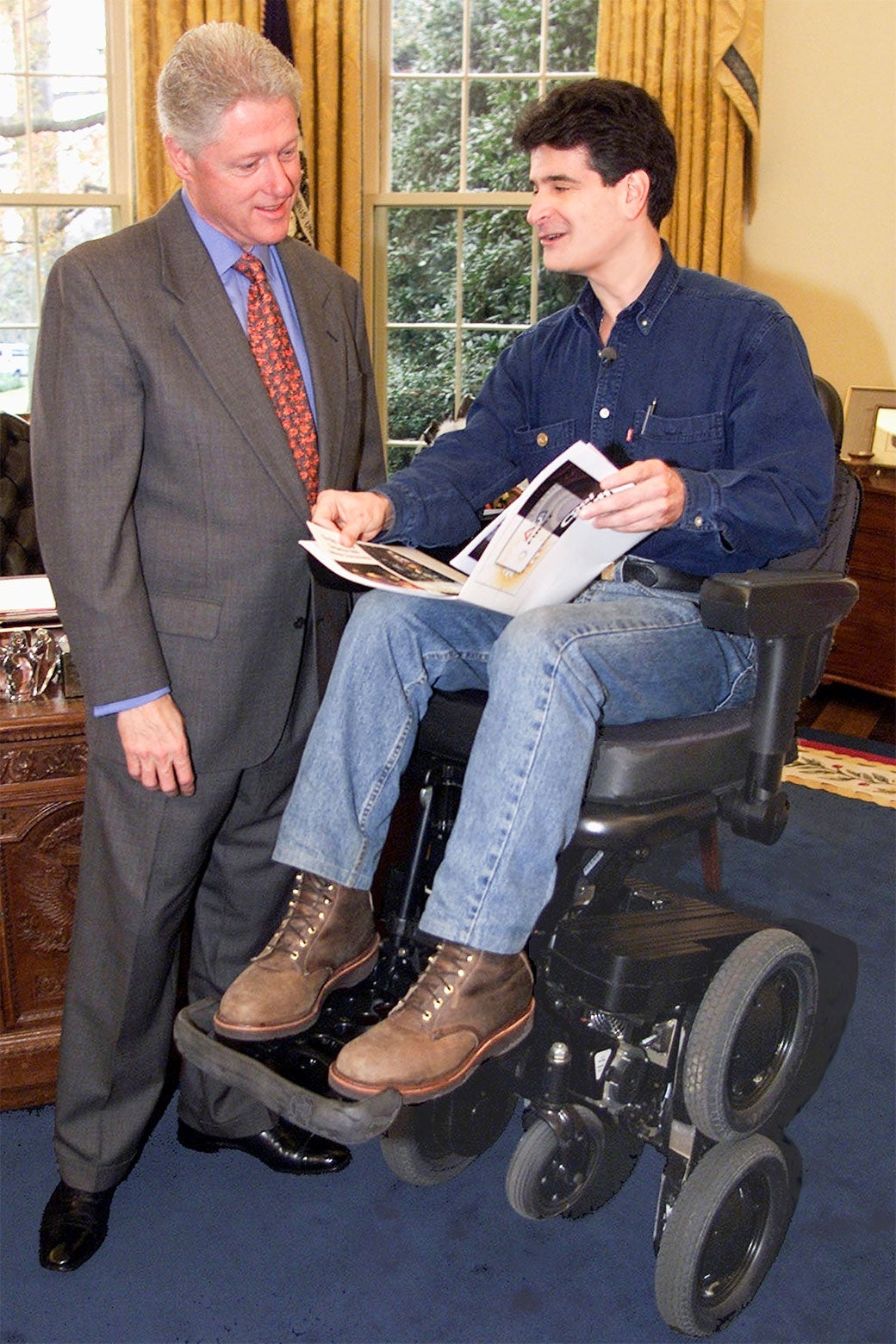 Dean Kamen sits in an iBot wheelchair in the Oval Office while showing a binder to Bill Clinton.
