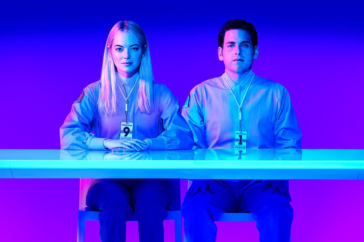 Emma Stone and Jonah Hill sit at a desk while wearing plain clothes and badges in this still from Maniac.