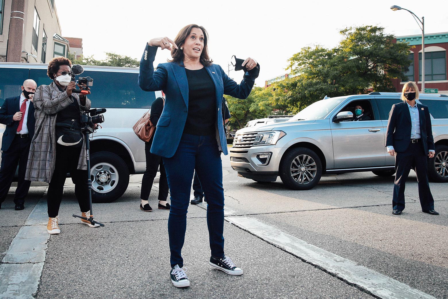 Harris, wearing a business casual outfit and Converse sneakers, stands on the pavement addressing supporters