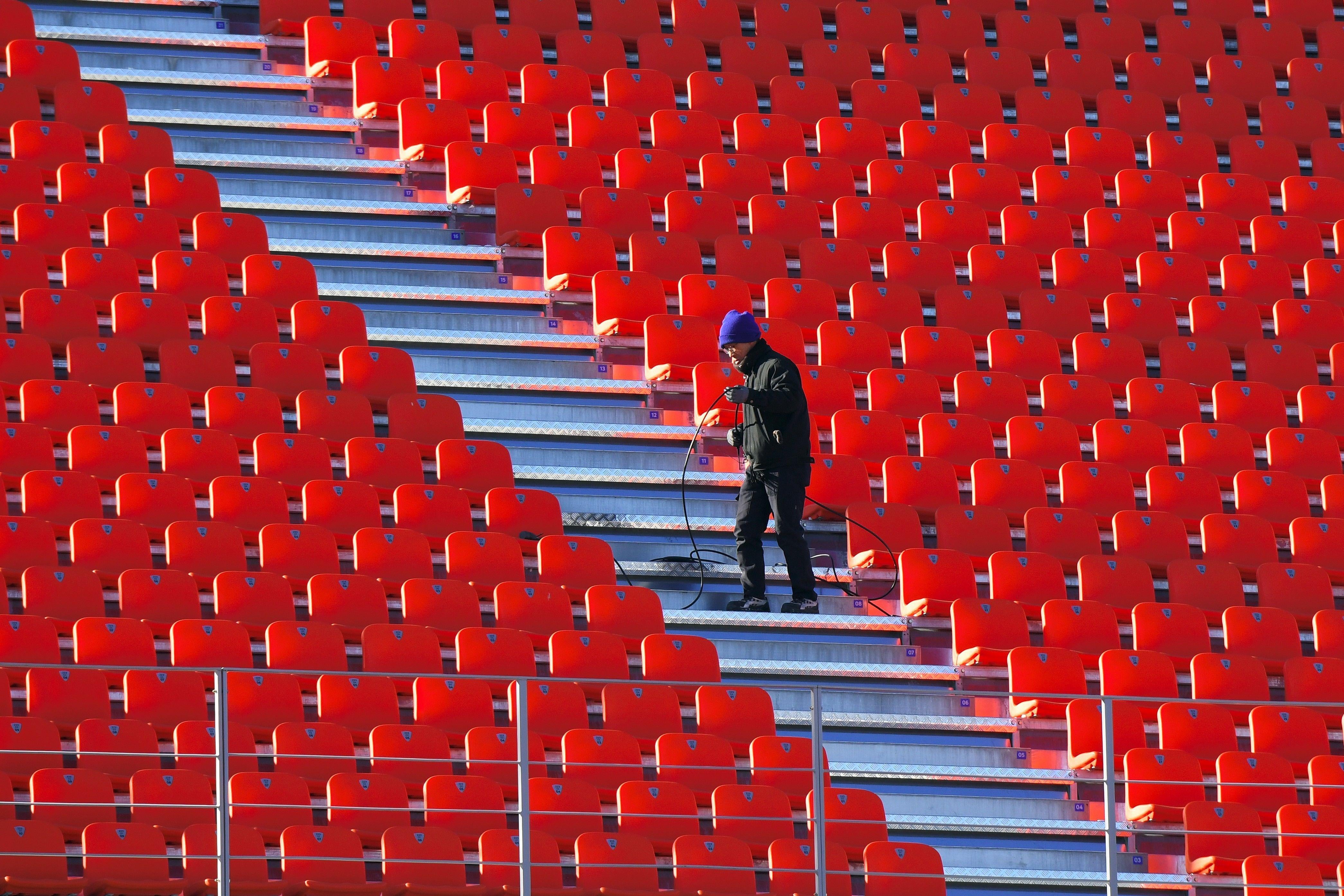 A lone worker sets up a cable at the Olympic Stadium in Pyeongchang, surrounded by a sea of empty, red seats.