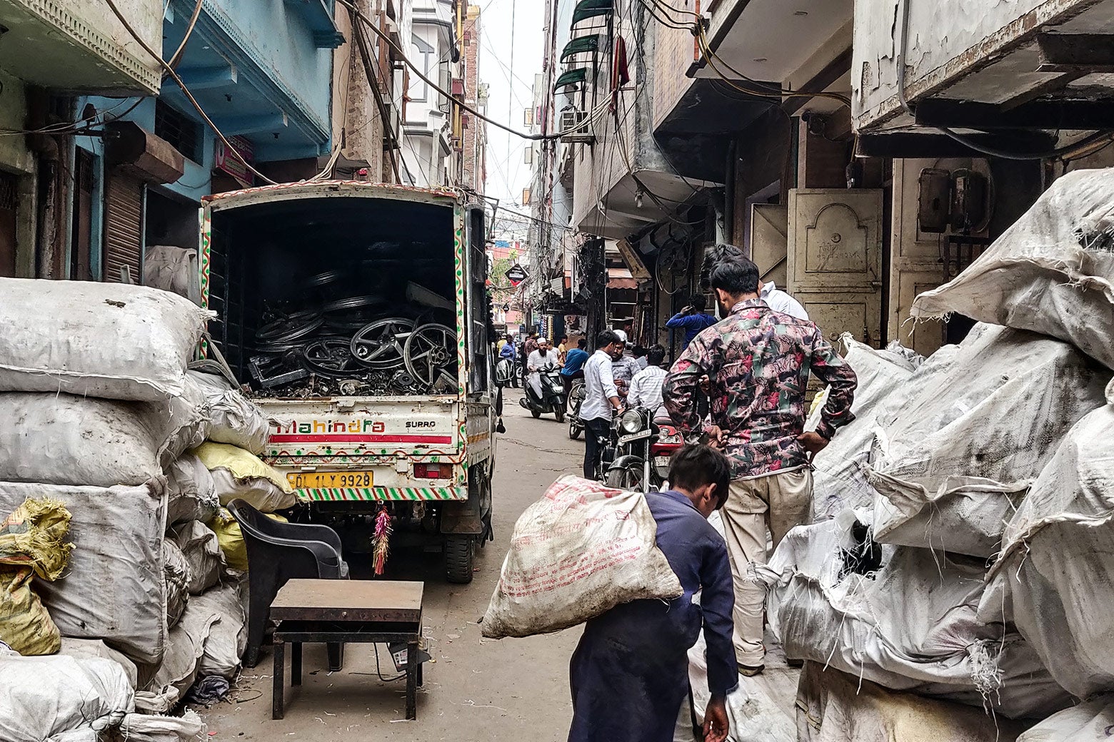 Tall buildings frame a crowded street, filled with white bags containing e-waste, and a truck with more waste. 