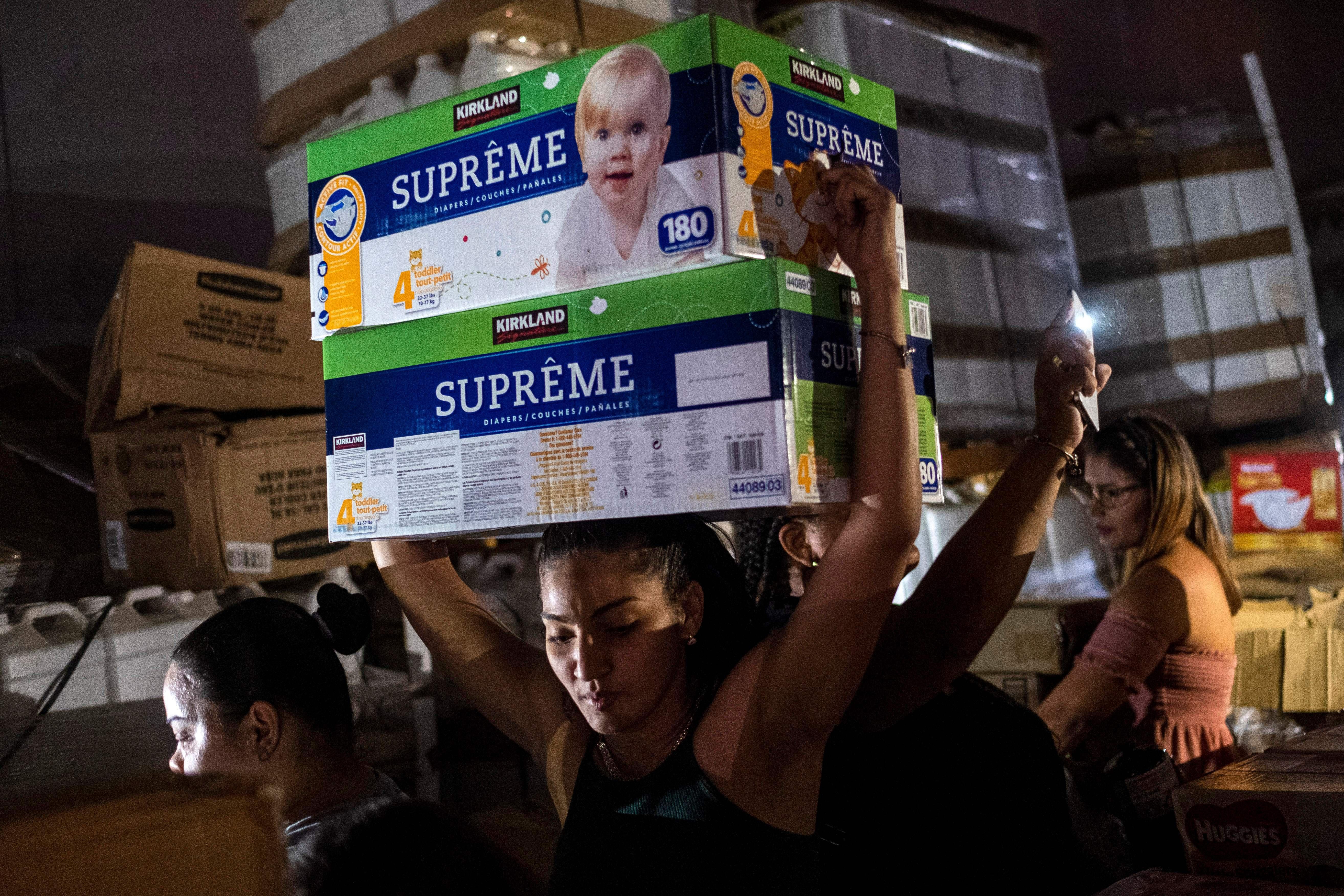 A woman carries boxes of baby diapers from warehouse filled with supplies, including thousands of cases of water, believed to have been from when Hurricane Maria struck the island in 2017 in Ponce, Puerto Rico on January 18, 2020.