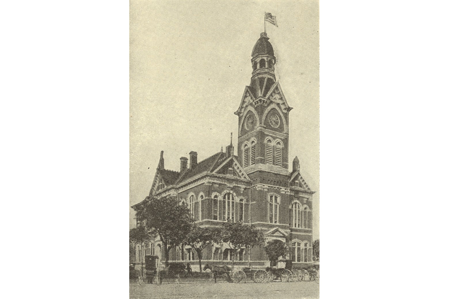 A brick city hall with an American flag flying.