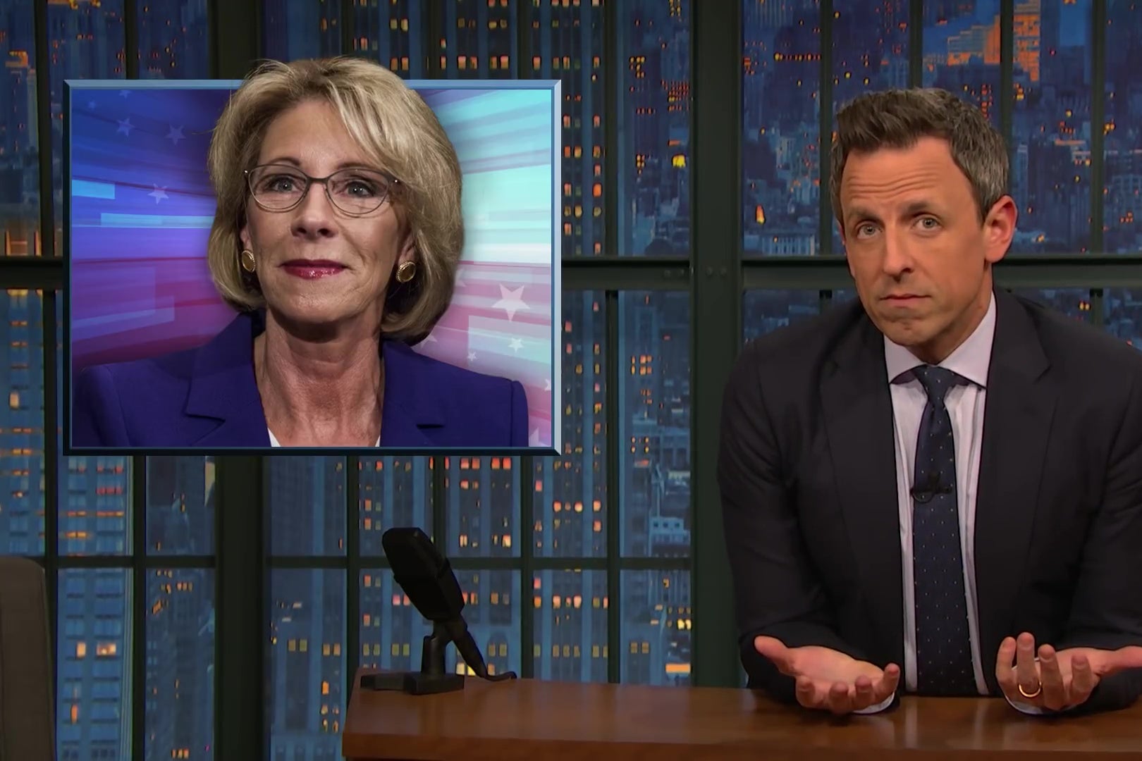Seth Meyers at an anchor desk, in front of a picture of Betsy DeVos.