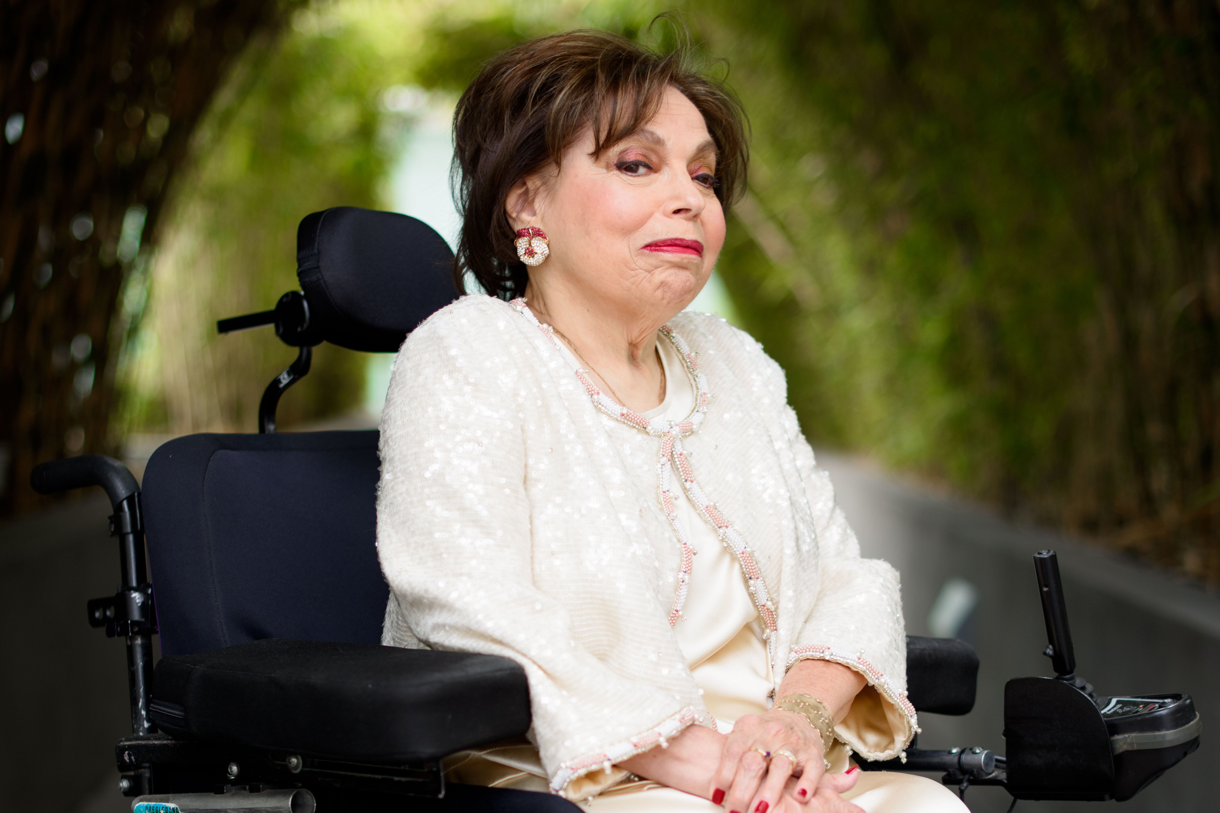 A woman in red lipstick and a wheelchair makes a close-lipped smile.