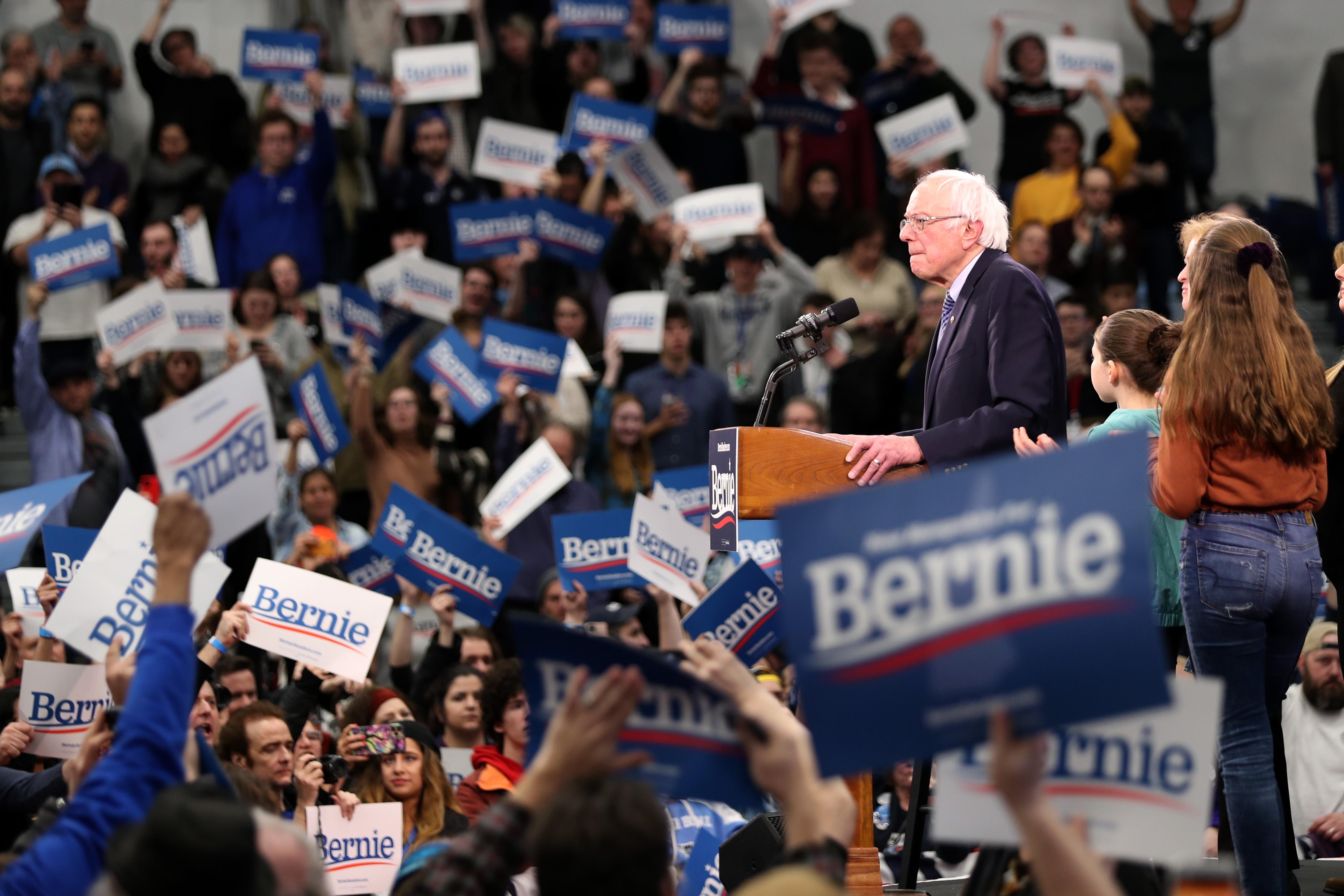 Bernie Sanders onstage speaking to supporters carrying signs with his name on them.