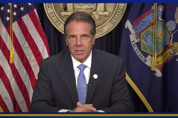 Cuomo sitting with the New York flag and American flag behind him.