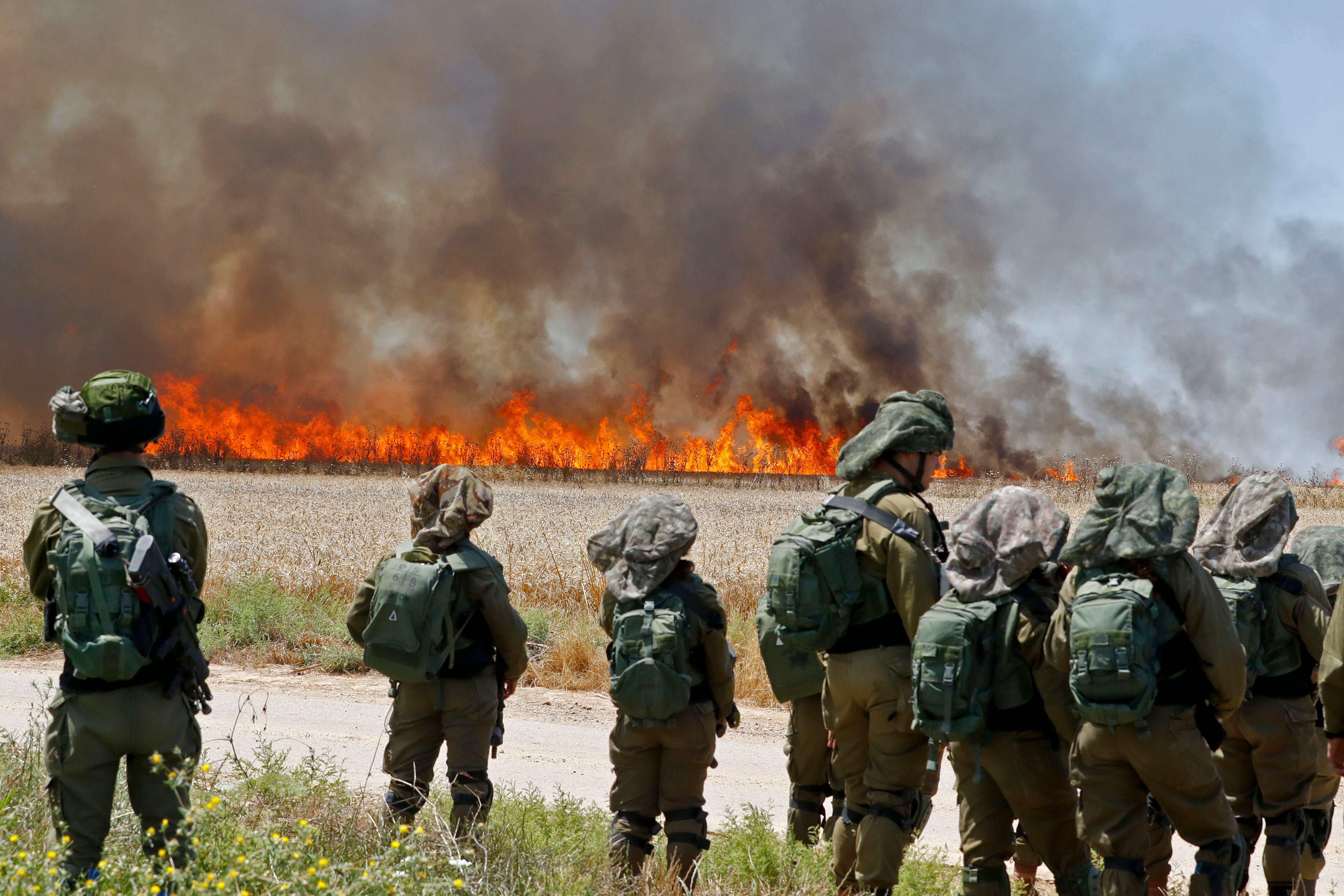 Israeli soldiers walk amid smoke from a fire in a wheat field.