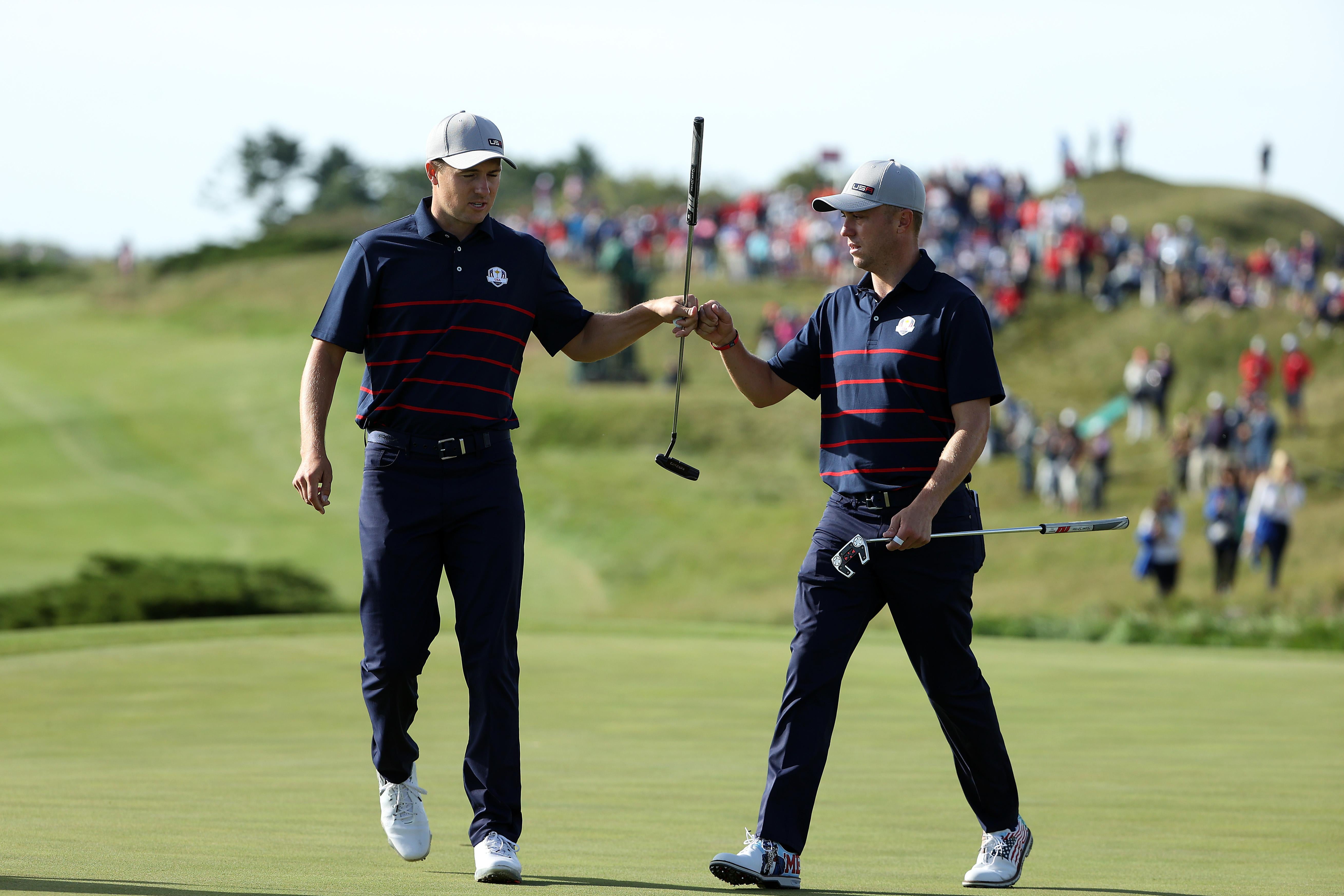 Jordan Spieth and Justin Thomas bump fists on the green of a golf course.