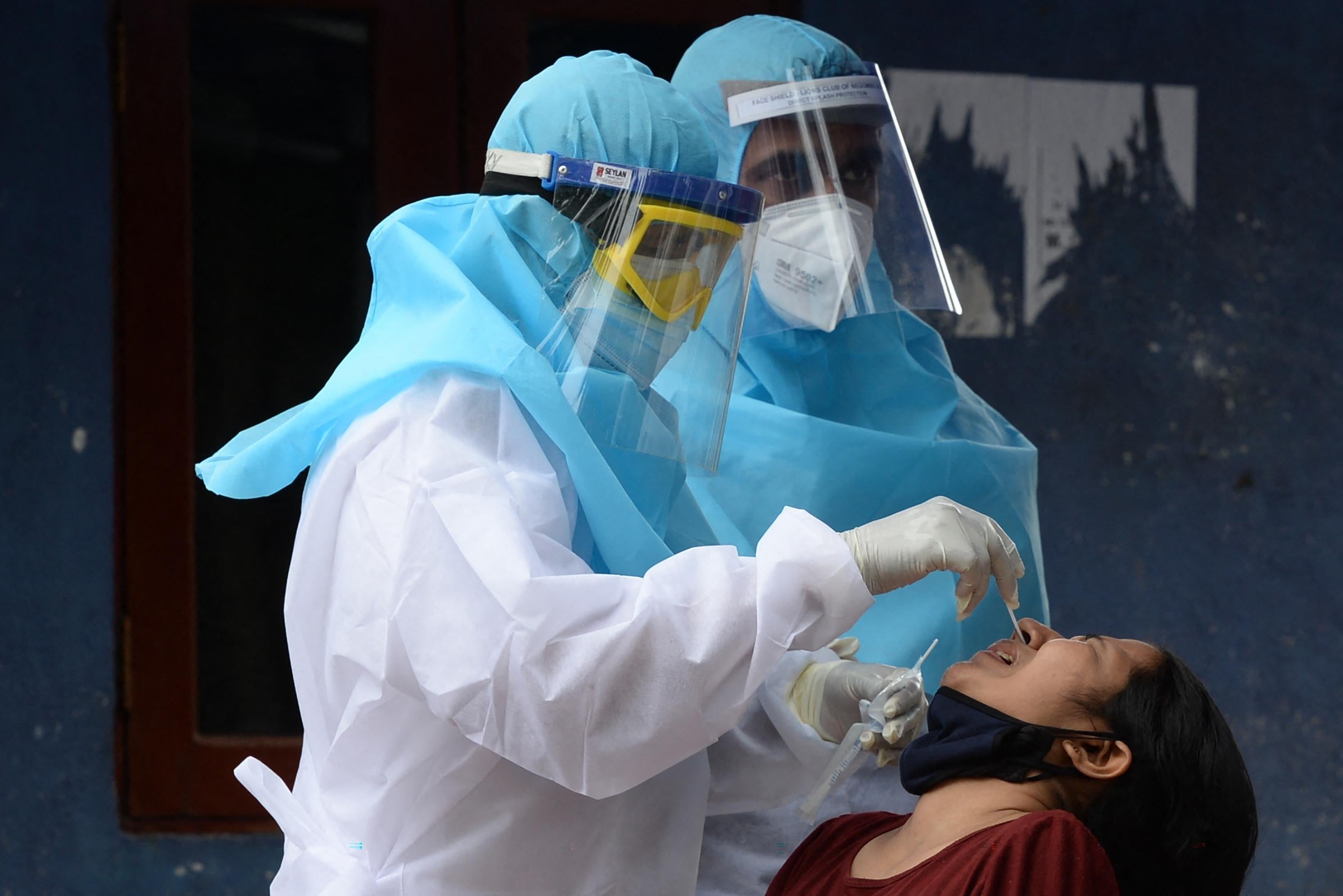 A medical worker wearing protective gear collects a swab sample from a woman sitting with her head back.