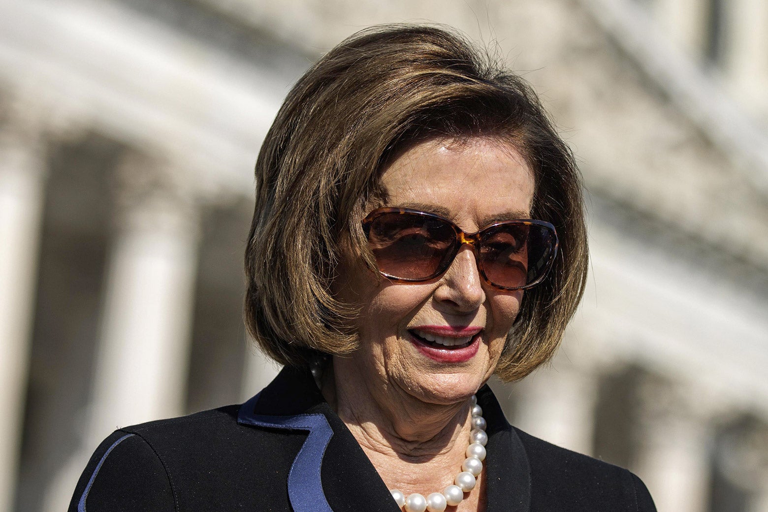 A photo of Nancy Pelosi, wearing sunglasses, standing in front of the Capitol.