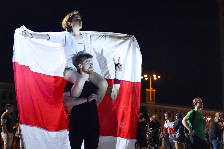 A young woman sits on a man's shoulders, draped in a red-and-white flag.