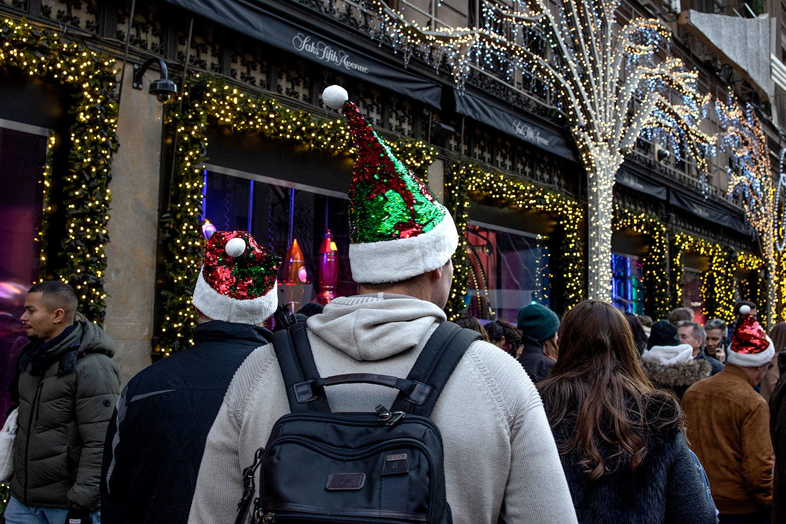 Shoppers on a holiday light-covered 5th Avenue in New York City. They have festive hats.