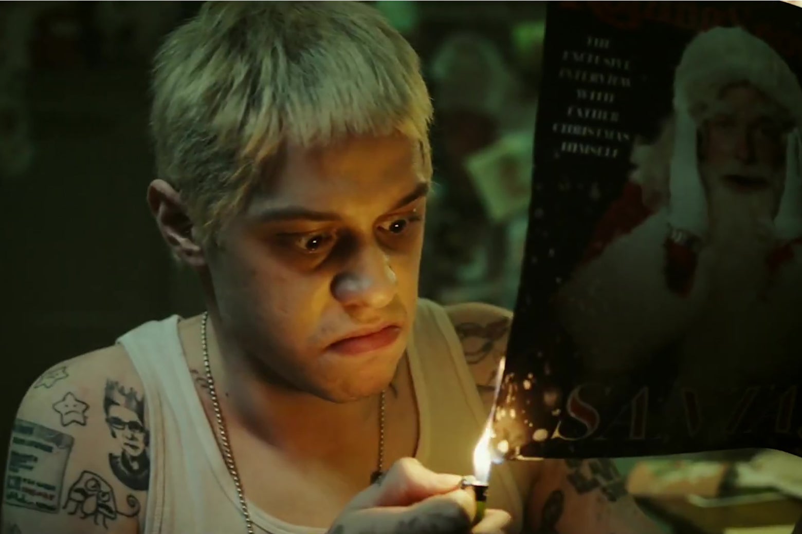 Pete Davidson, with his hair died blonde like Eminem, sets a photograph of Santa Claus on fire.