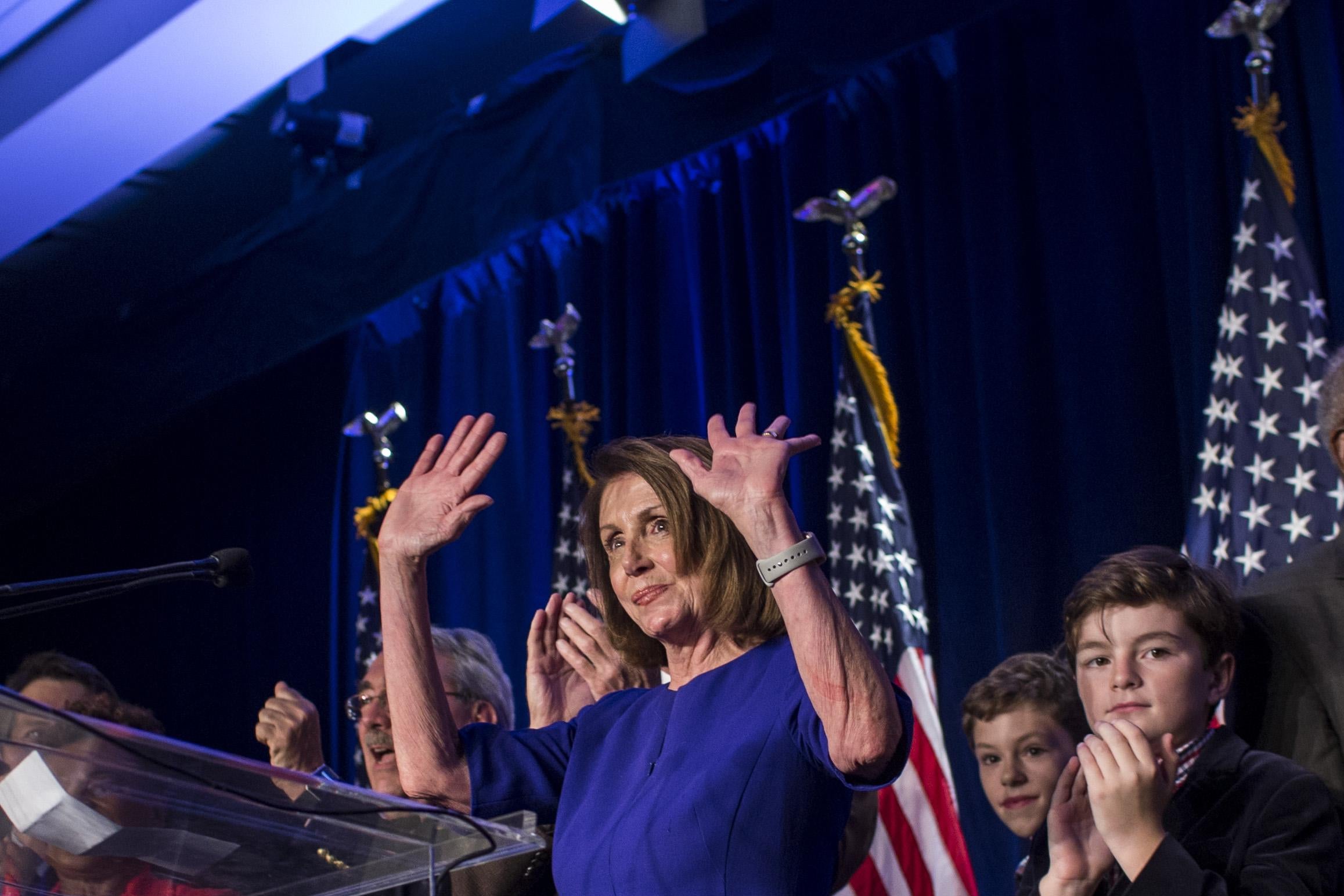 Nancy Pelosi raises her hands from behind a podium.
