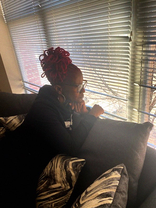 Koumba Yasin, seated on her couch, looks out of her sunny window.