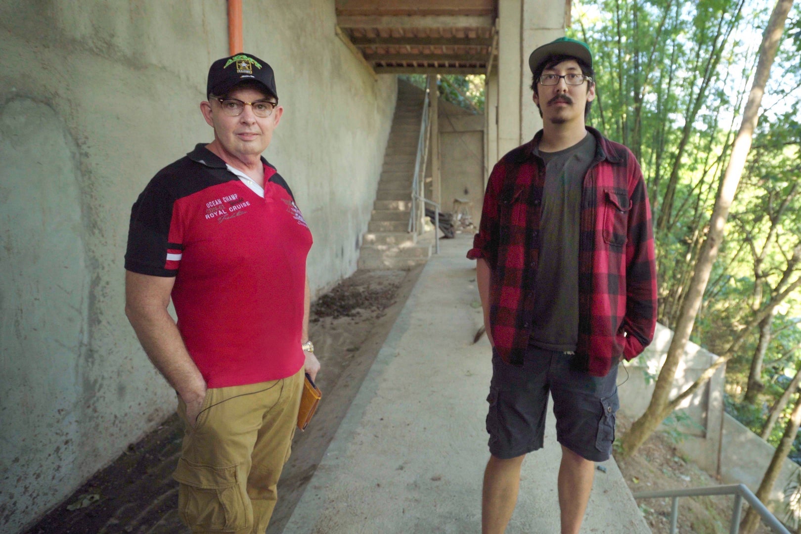 Jim and Ron Watkins look at the camera as they stand on a concrete walkway on a pig farm.