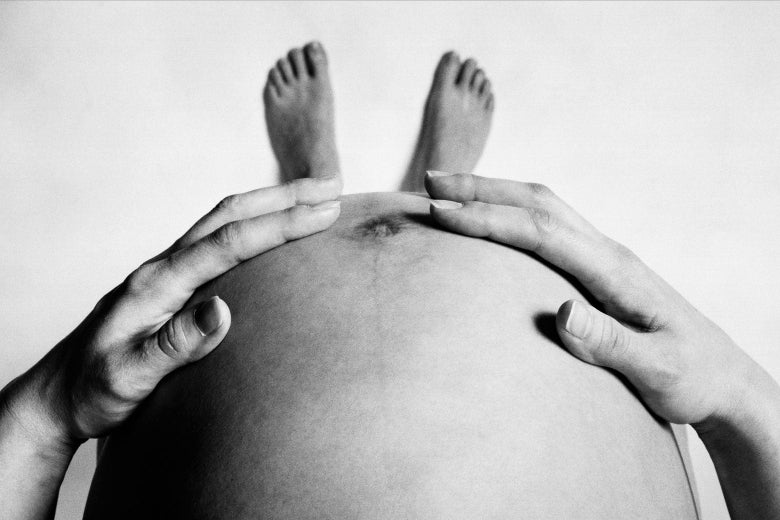 A woman looks down at her pregnant belly.