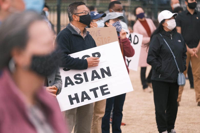 Masked people standing in a park. One man holds a sign that says "Stop Asian Hate."