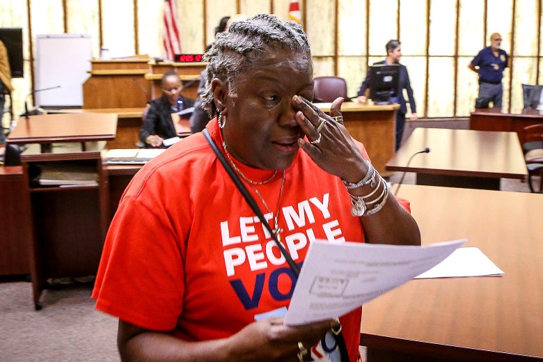 A woman holds a piece of paper in one hand and wipes away a tear from her eye with the other.