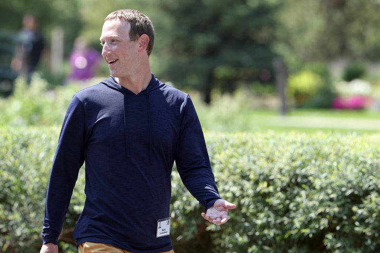 Mark Zuckerberg walks in front of a line of hedges while looking and talking toward his right.