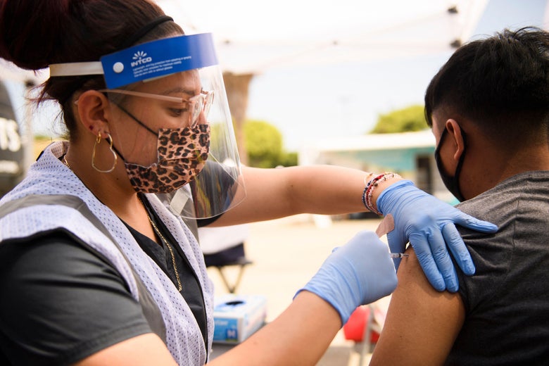 A medical professional wearing a face shield and gloves administers a vaccine to a teen