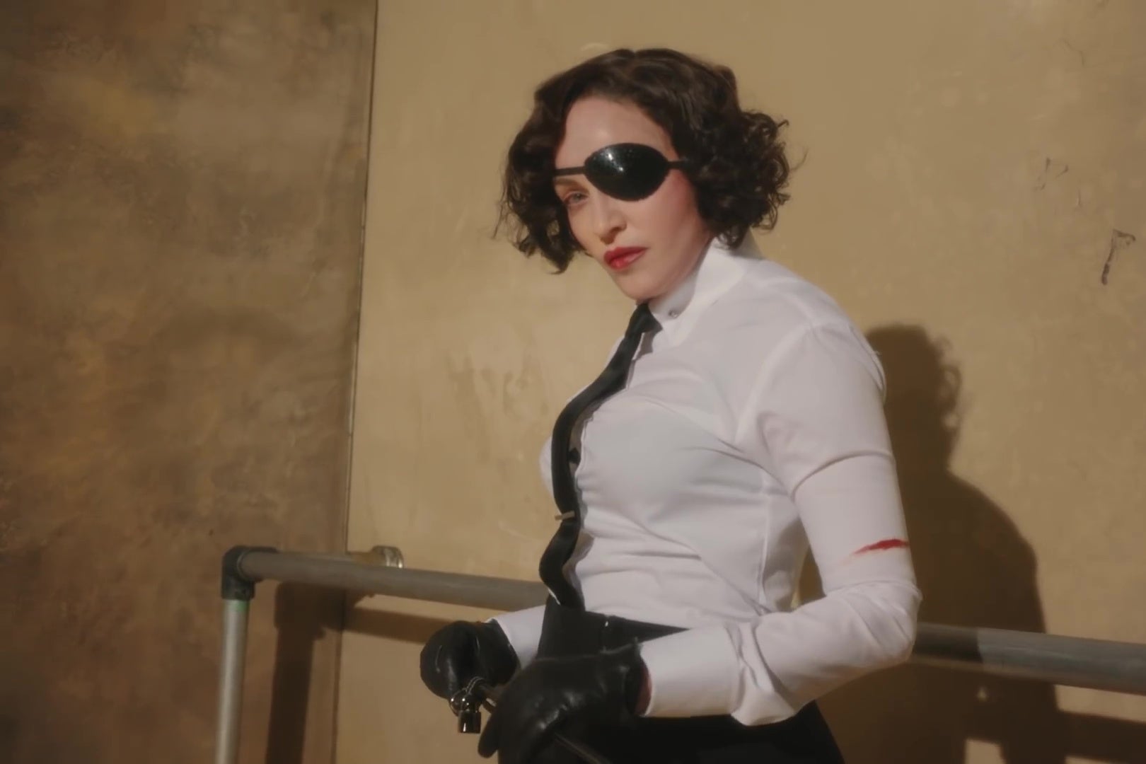 Madonna, in a white dress shirt, black tie, black eyepatch, and black leather gloves.