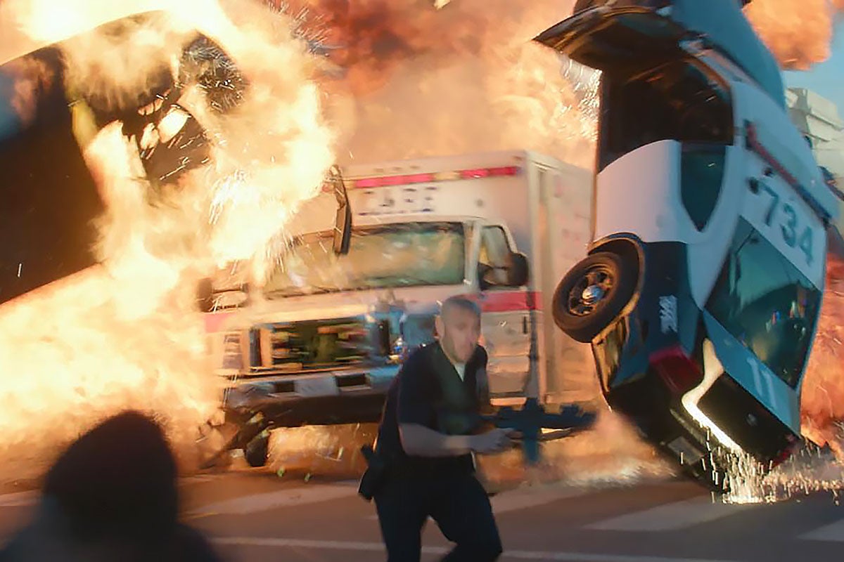 An ambulance driving between two cars exploding in a scene from the movie