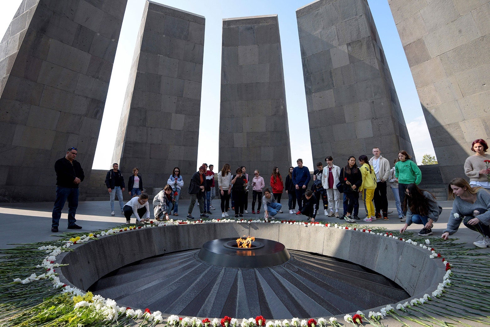 Armenians gathered around a commemorative flame, with tall stone slabs in the background.