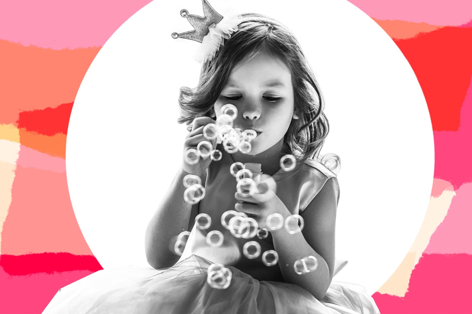 A girl blows bubbles while wearing a princess dress and crown.