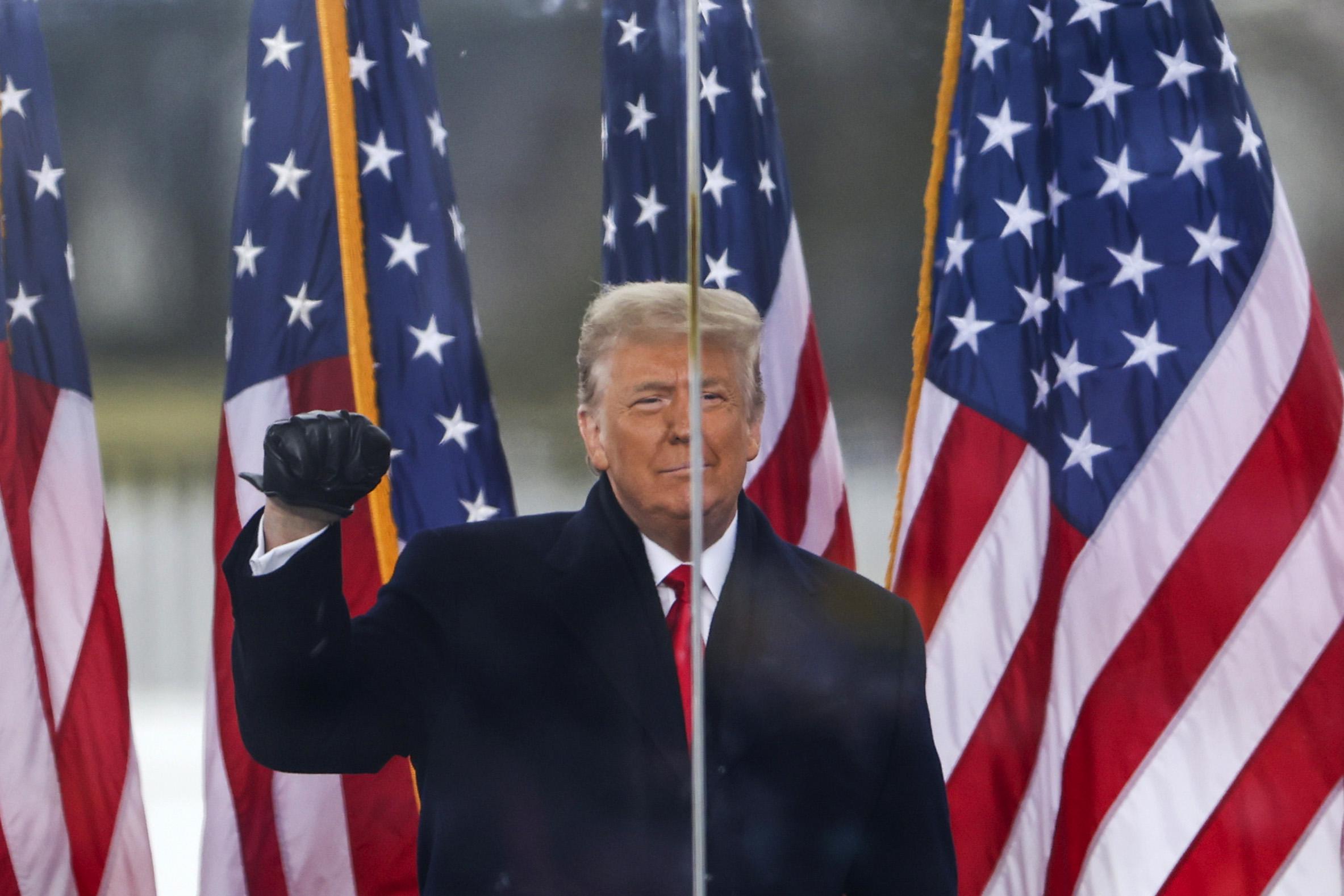 Trump smiles and makes a fist, standing onstage in front of American flags