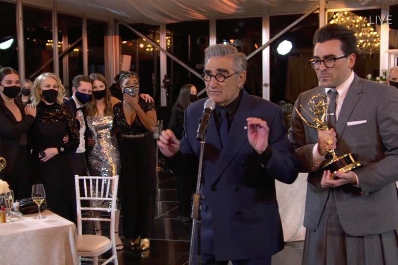 Eugene Levy and Dan Levy stand at the microphone as their Schitt's Creek comrades look on in masks.