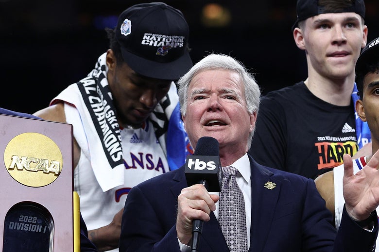 Emmert speaks into a microphone with Kansas players around him and the trophy to his right