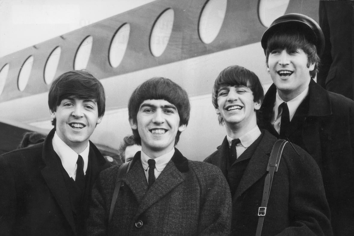 The Beatles, in black and white, standing in front of an airplane.