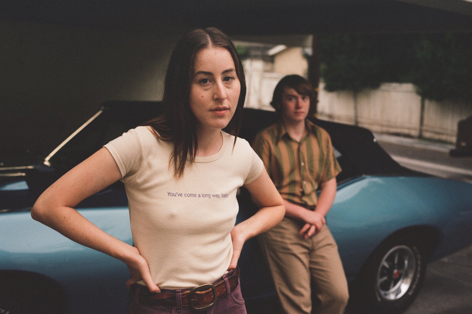 She wears an off-white t-shirt and purple cords and looks defiantly at the camera. In the background, out of focus, he leans against a car, in a very '70s buttondown and khakis, his hands casually crossed over the front of his pants.