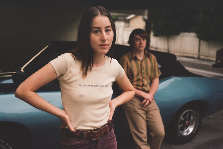 She wears an off-white t-shirt and purple cords and looks defiantly at the camera. In the background, out of focus, he leans against a car, in a very '70s buttondown and khakis, his hands casually crossed over the front of his pants.