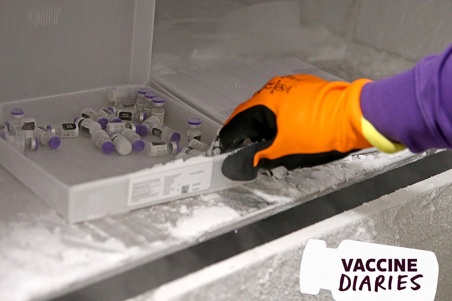 A gloved hand pulls COVID-19 vaccine vials out of a freezer.