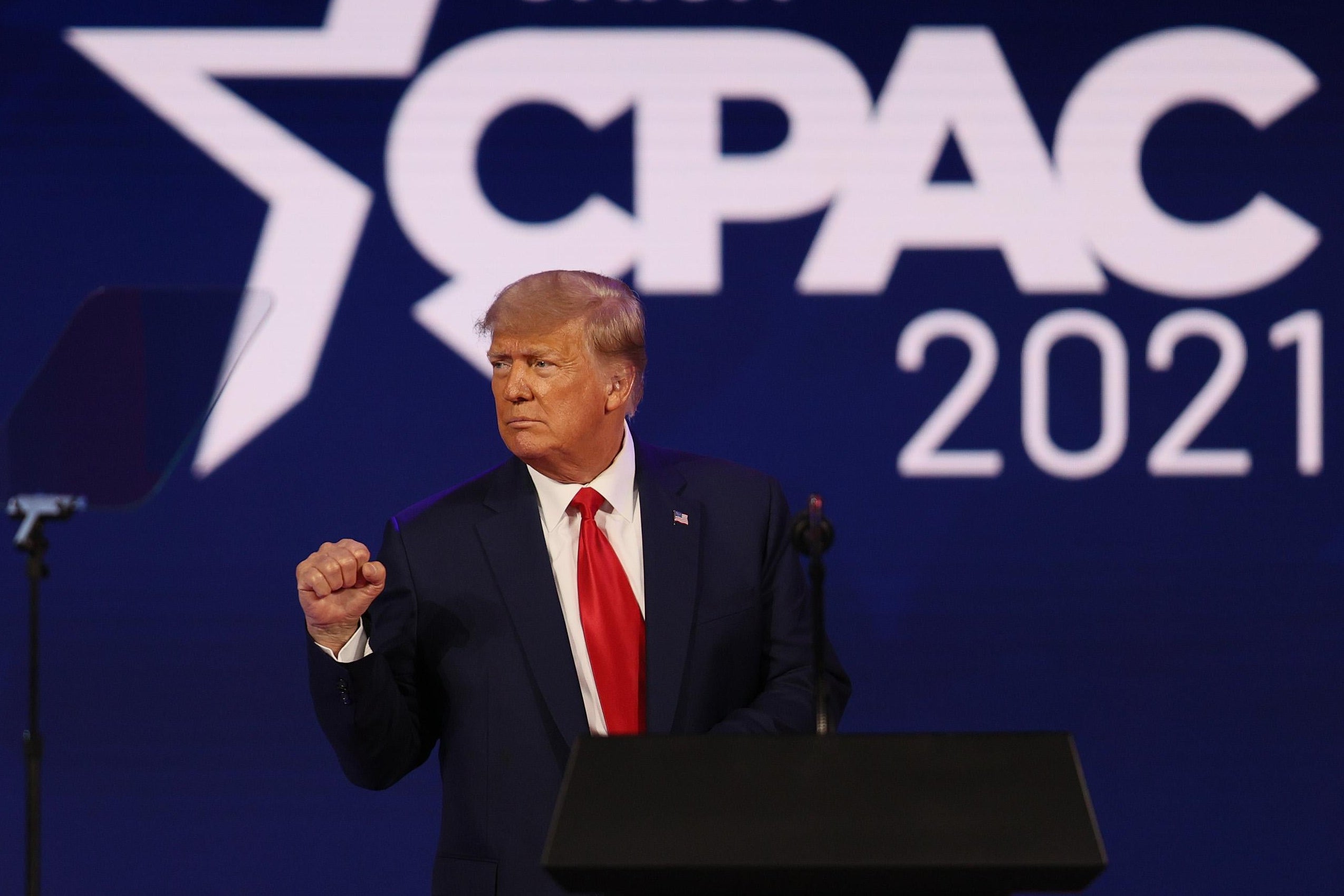 Trump pumping his fist onstage with the CPAC 2021 logo behind him